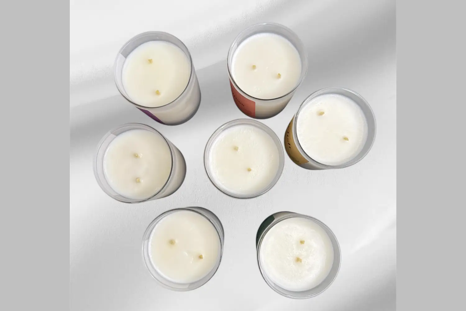 A collection of six scented candles with white wax and varying colored labels, arranged in a circular pattern.